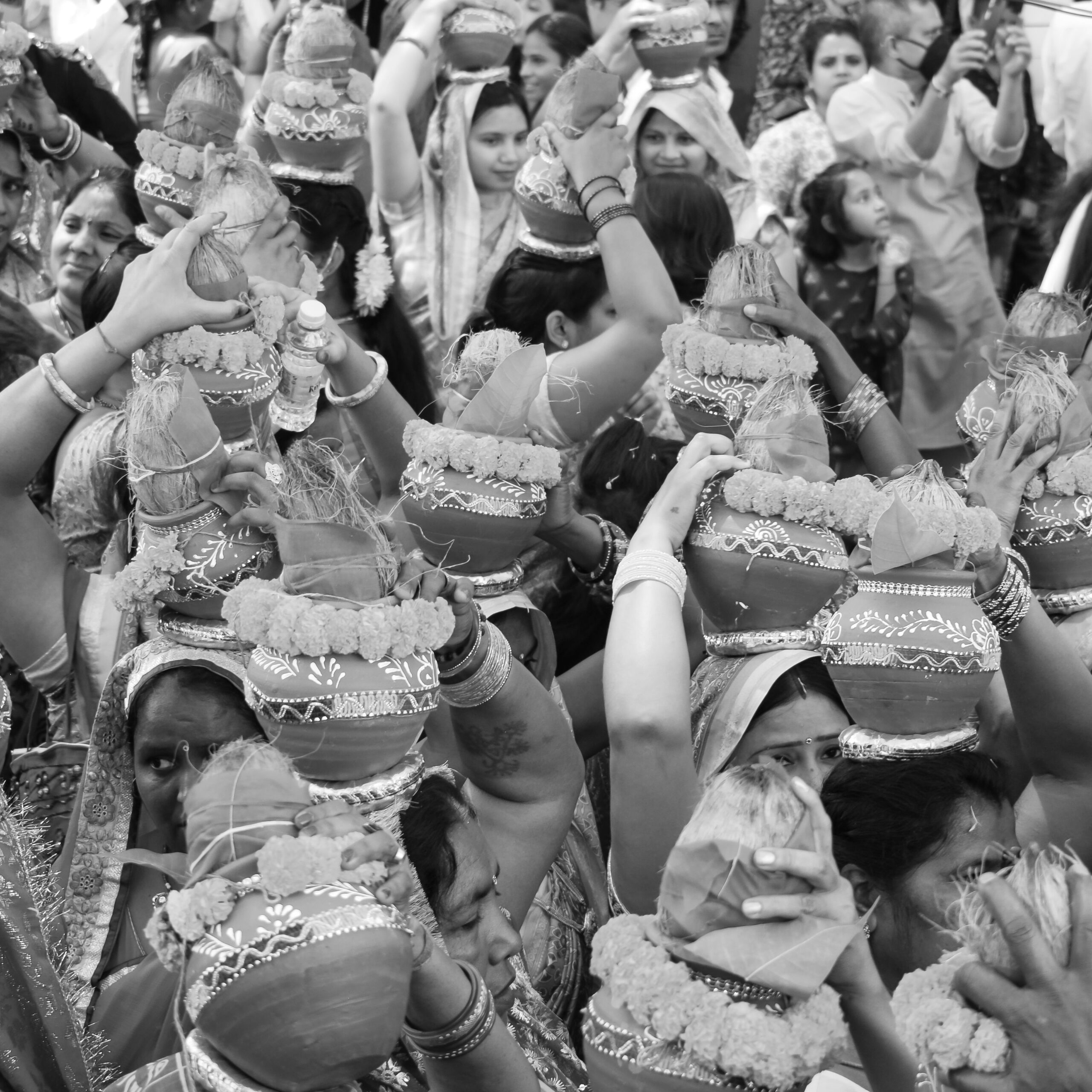 Black and white capture of women celebrating a traditional Indian festival, carrying decorated pots.